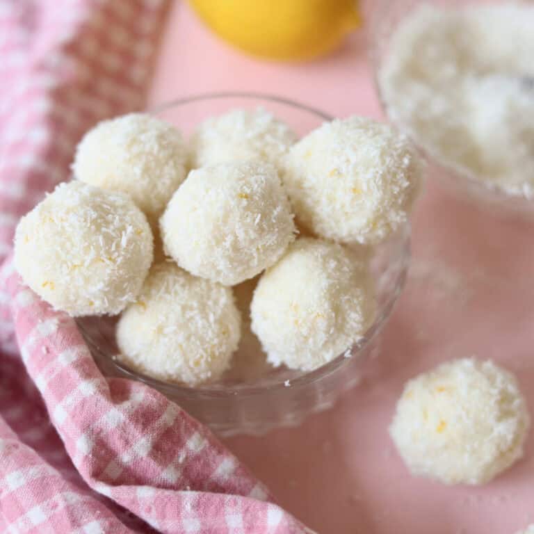 A small glass bowl overflowing with lemon coconut truffles, ready to eat.