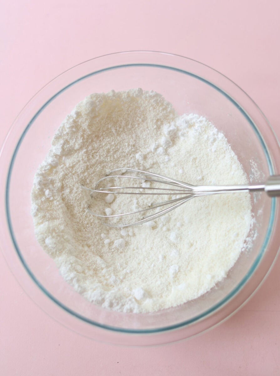 Coconut and icing sugar in a glass bowl with a whisk ready to mix together.