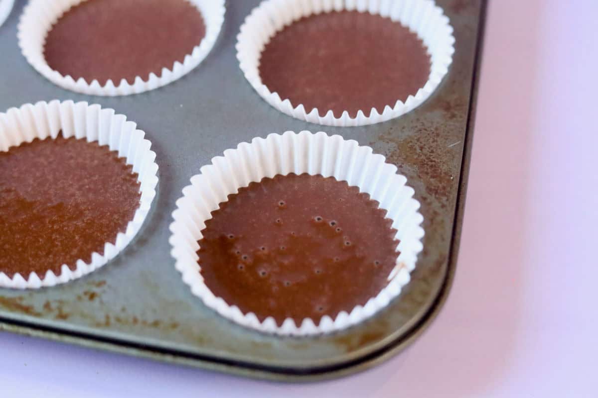 A close up of the chocolate cupcake batter in cupcake liners, ¾'s filled.