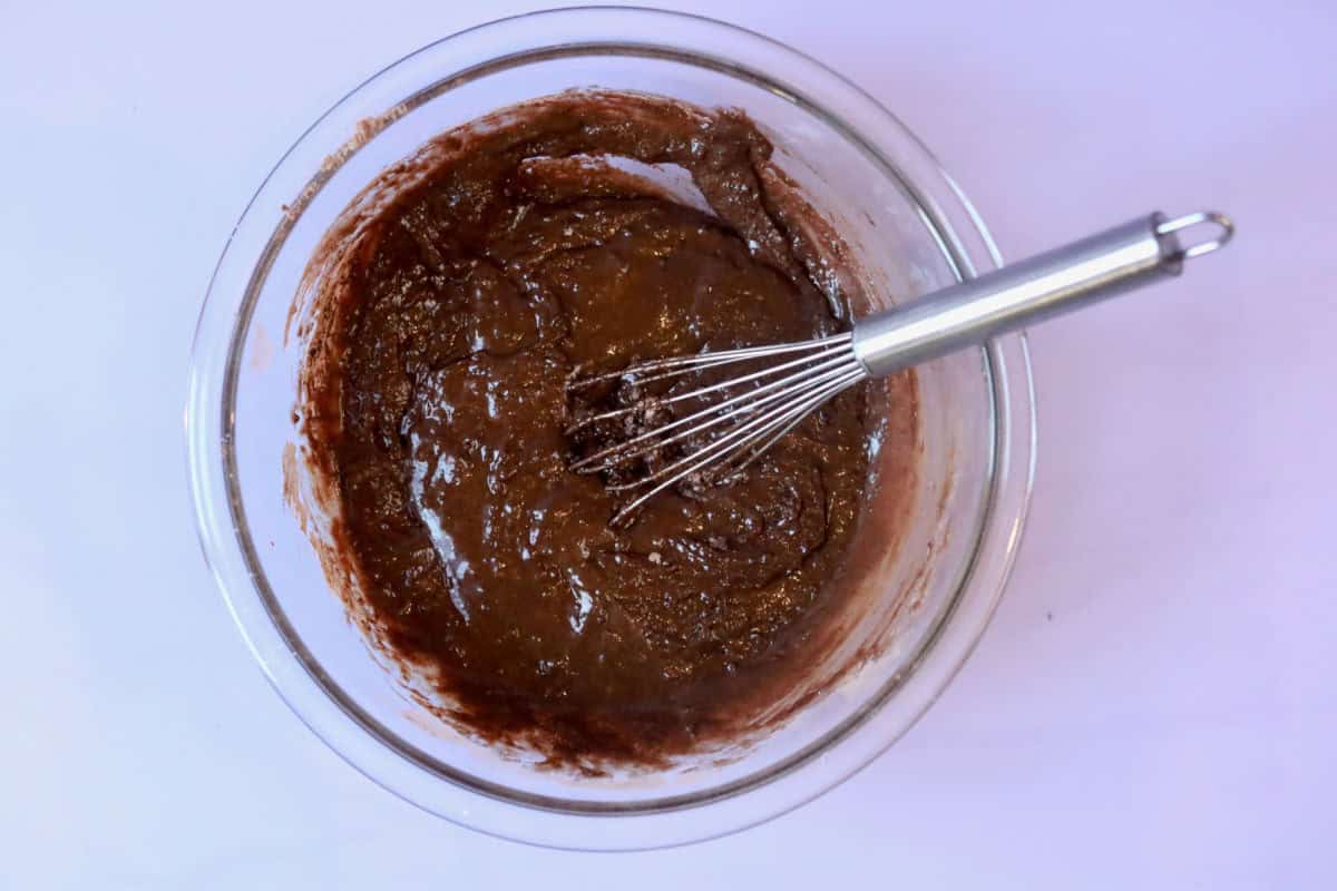 Dry and wet ingredients mixed together before the hot water has been added in a glass bowl with a whisk.