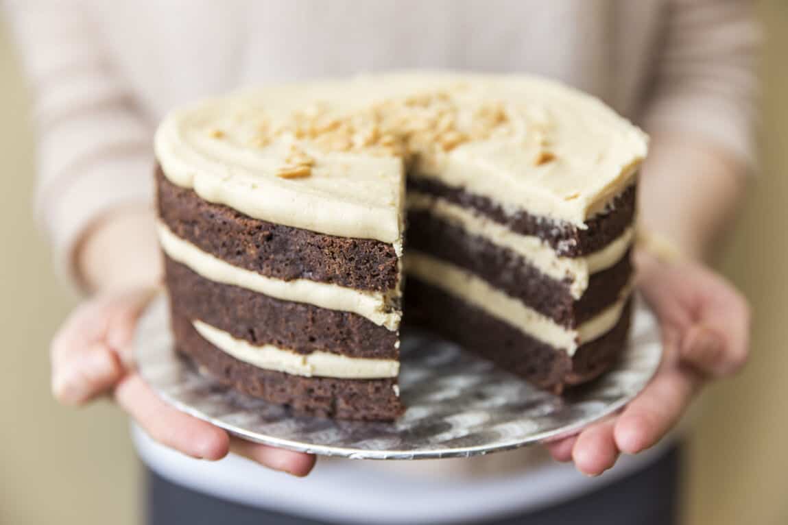 A person holding the chocolate layer cake with peanut butter buttercream. Two cake slices have been cut out of it.