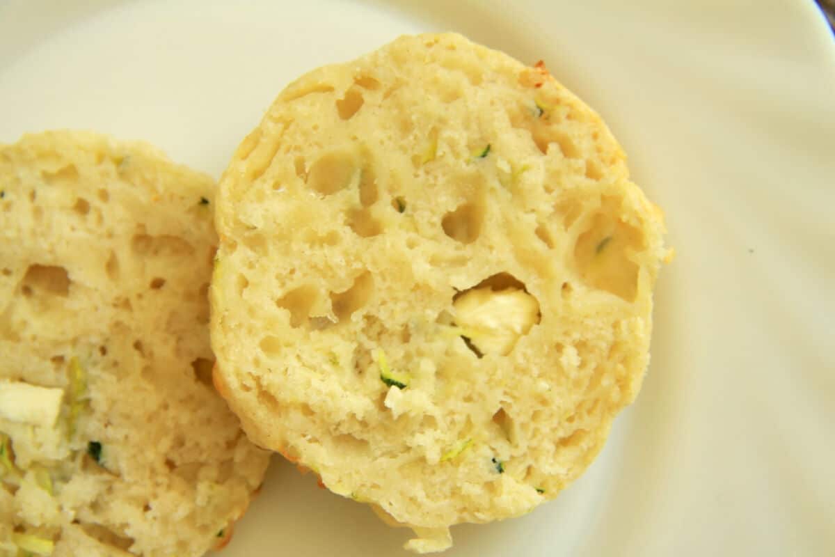 A feta and zucchini scone cut in half to reveal the soft and fluffy texture. Nuggets of feta can be seen. Yum!