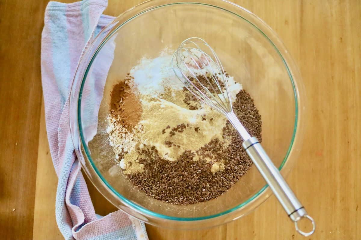The dry ingredients for the lactation cookies have been poured into a glass bowl and a whisk is in the bowl.
