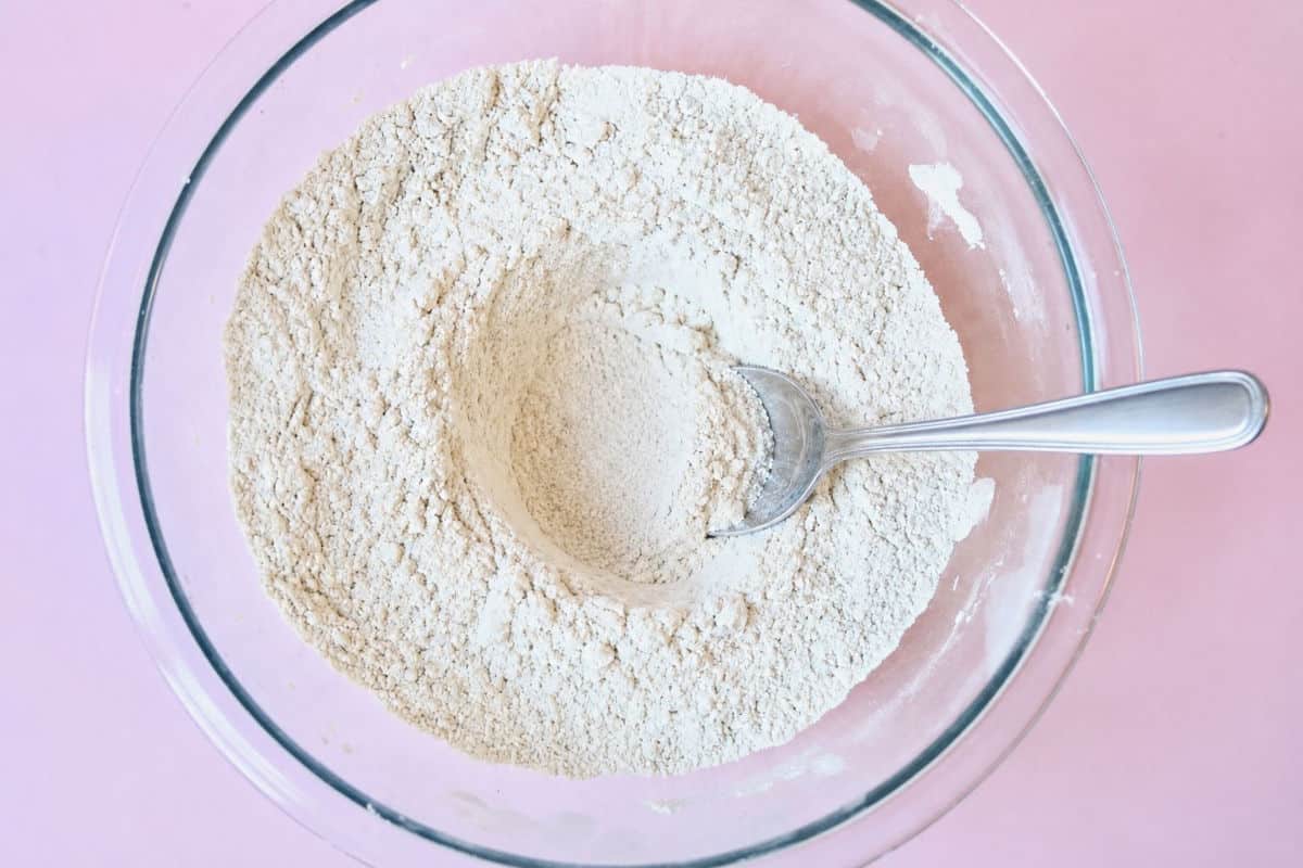 Dry ingredients with a metal spoon which has made a well in the middle of the dry ingredients.