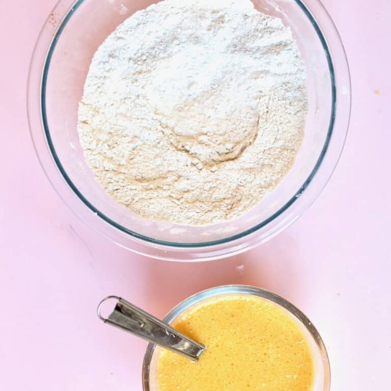 Two glass bowls on a pink board. One larger bowl has dry ingredients for a muffin recipe and the other has wet ingredients. In preparation for baking using the muffin method.