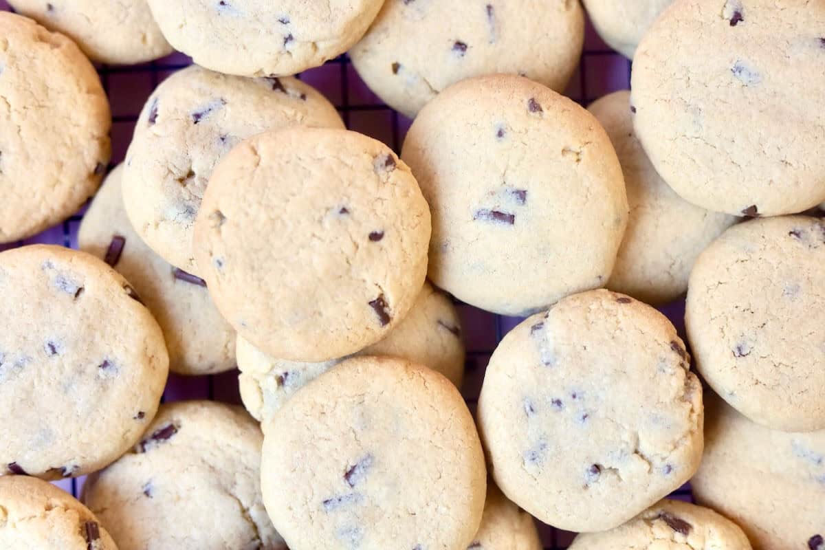 Big batch of chocolate chip cookies cooling on a wire rack. The cookies looks perfectly golden brown with flecks of the chocolate chips coming through.
