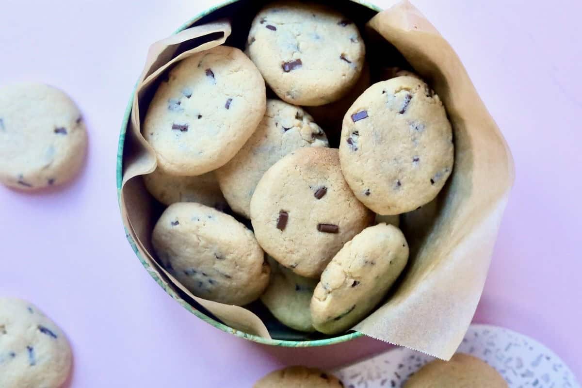 A cookie tin lined with baking paper and filled with chocolate chip cookies.