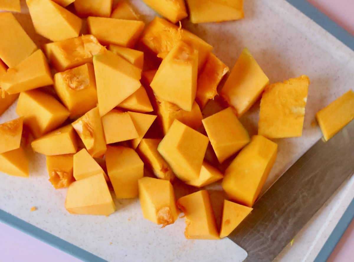 A chopping board and knife with chopped up pieces of pumpkin.