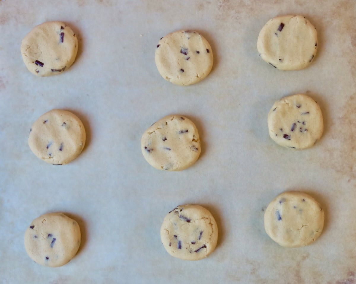 Chocolate chip cookie dough which has been rolled and pressed into cookie balls, on a baking tray.
