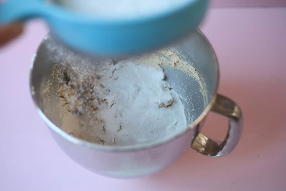 A blue sieve is sifting the dry ingredients on top of the creamed mixture.