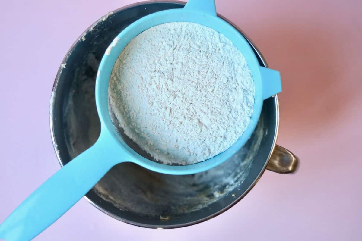 A mixing bowl with creamed butter and sugar with a sieve of dry ingredients on top.